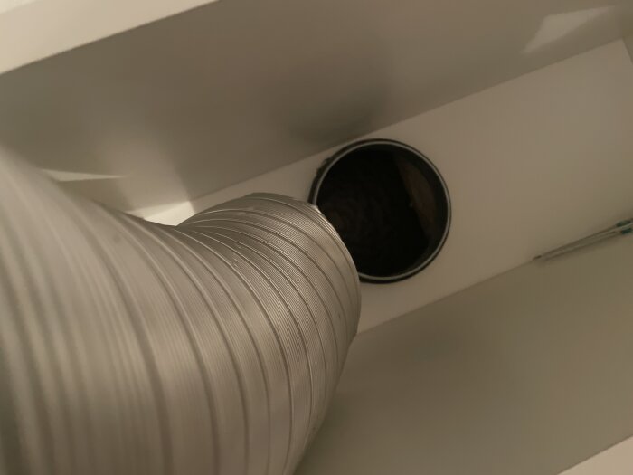 Flexrör försöker anslutas till stos i skåp, liten misspassning finns mellan delarna.