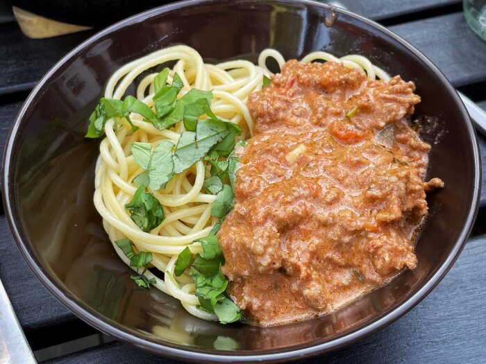 Skål med spaghetti och köttfärssås, toppad med gröna örter.