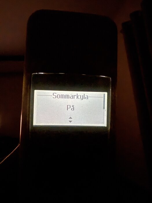 Fjärrkontrollens display visar texten "Sommarkyla På" i en mörk miljö.