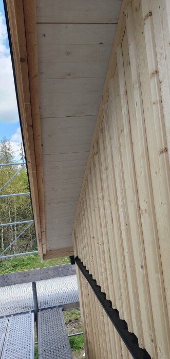 Råsponttak och träpanel på ett nybyggt hus, med byggnadsställning i bakgrunden.