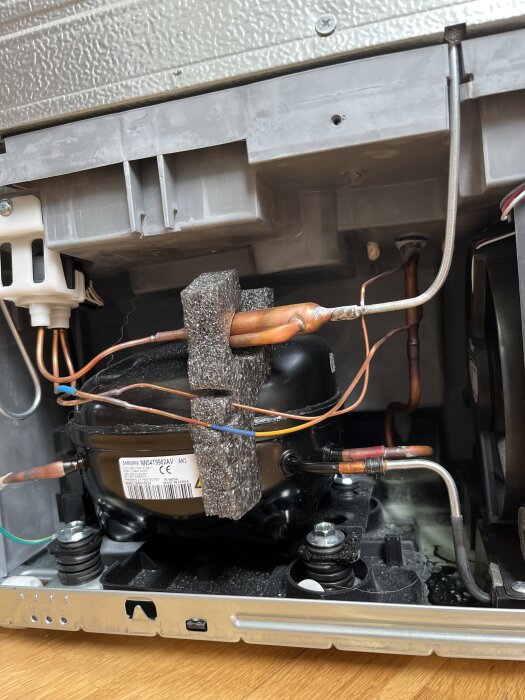 Kompressor och kopparrör inuti en apparat med synliga elektrokablar och fläkthjul. Inga tecken på avdunstning eller gummiproppar.