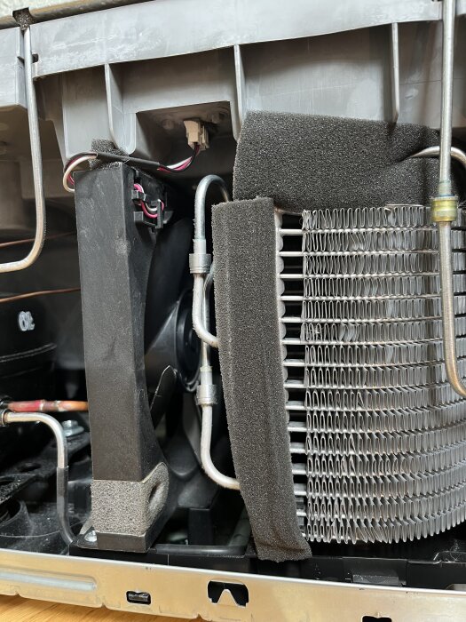 Kompressor och fläkthjul med stillastående delar, elkablar synliga; ingen synlig avdunstningsdel eller gummipropp i närheten.