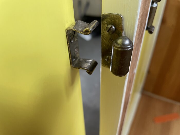 Ett kulsnäpplås på ett funkisskåp från 1940-talet med gul färg, där låsanordningen på dörrkarmen är i fokus.