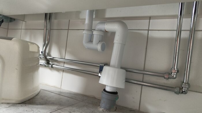 Avloppsrör under handfat med vattenlås och vakuumventil på plats i badrummet, anslutet till flera kromade rör.