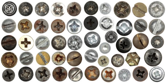 Olika typer av skruvskallar i flera material och färger, uppvisade i rader. Skruvarna har varierande mönster och slitage.