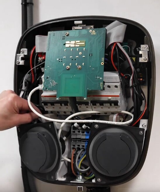 Bilden visar insidan av en laddbox från Charge Amps Aura, med synliga elektriska komponenter och anslutningar, inklusive dvärgbrytare och kablar.