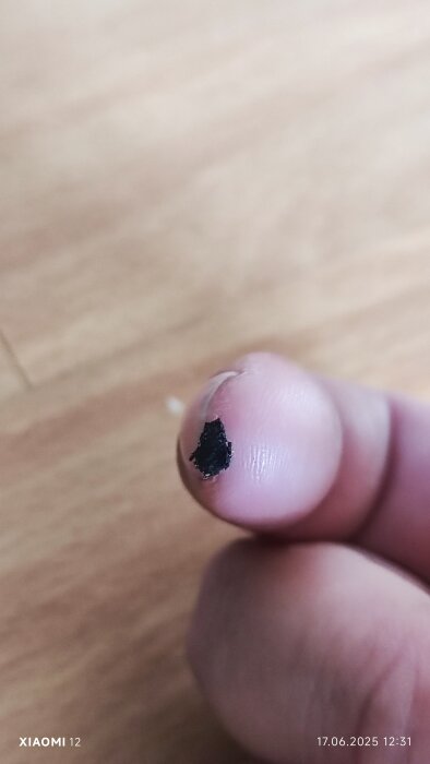 En närbild på ett finger med ett litet svart korn på fingertoppen, mot en suddig bakgrund.