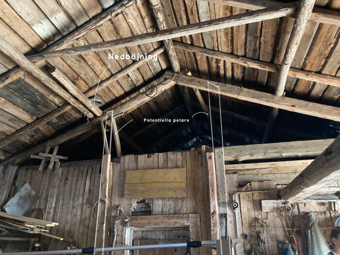 Interior of an old barn showing wooden roof structure with sagging beams and potential support pillars, highlighting structural challenges.