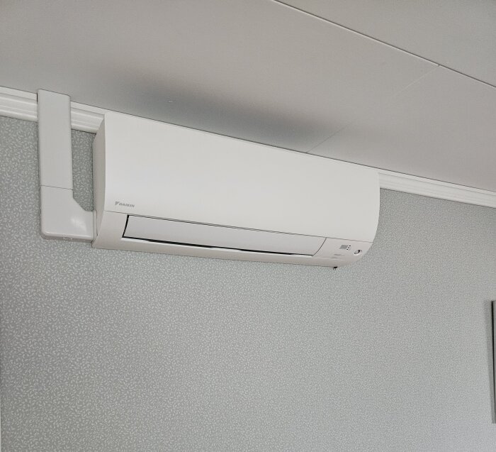 Luftkonditioneringsenhet monterad högt på en innervägg, vit och rektangulär med enkel design.