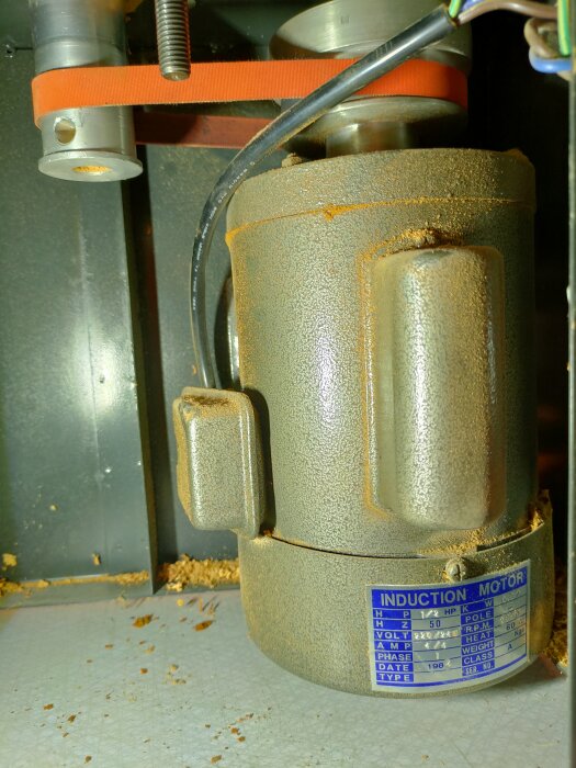 Gammal vertikalfräs med induction motor, röd rem och märkplatta. Lite smutsig verkstadsmiljö syns i bakgrunden.