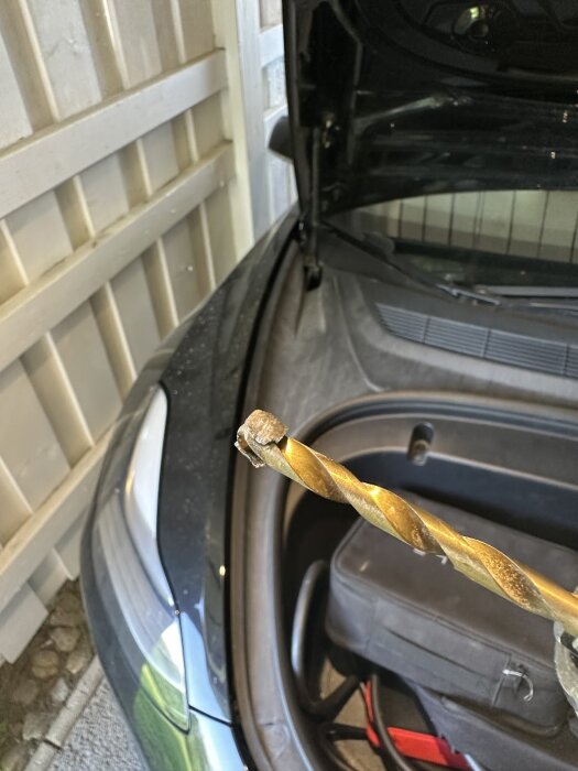 Borrspets visas framför en bil med öppen motorhuv, omgiven av ett garage.