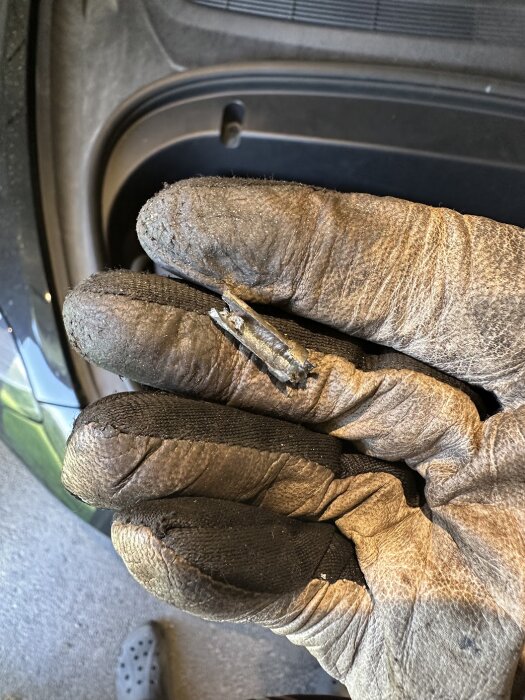 En hand med smutsiga arbetshandskar håller i en trasig metalldel, troligen en uttagen expanderande ring.