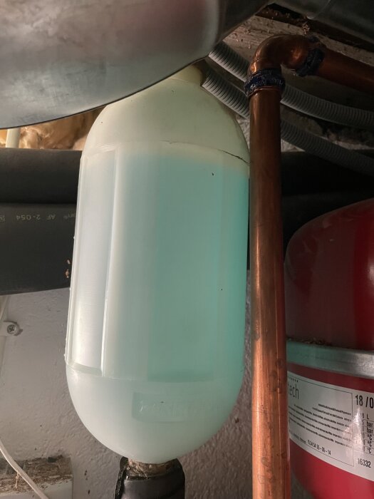 En vit behållare med grön vätska, ansluten till en kopparledning, del av ett värmepumpsystem.