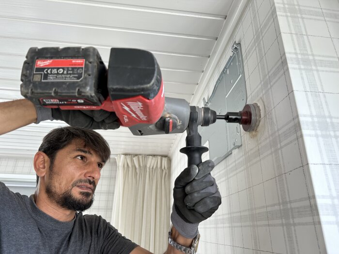 Man borrar ett hål i väggen med en borrmaskin för att installera en luftkonditionering i sovrummet.