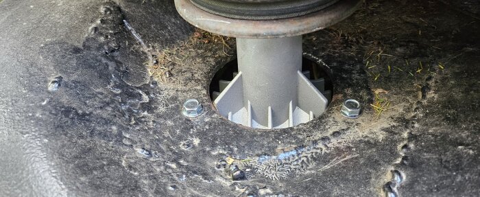 Närbild av gräsklipparens knivspindelhus, nytt och installerat med synliga fästbultar och omgivande gräsklipp.