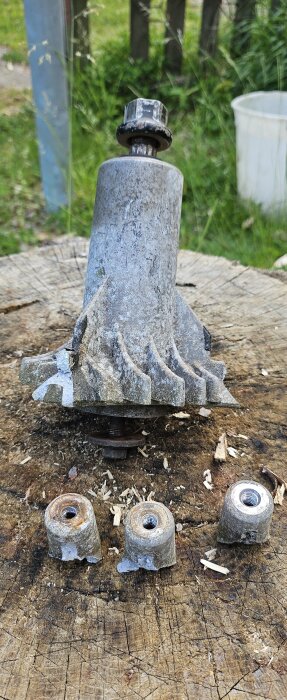 Trasigt knivspindelhus från gräsklippare med avbrutna fästöron, liggande på en stubbe.