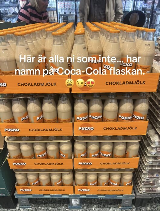 Flera flaskor Pucko chokladmjölk staplade i en livsmedelsbutik, med hänvisning till brist på namn på Coca-Cola-flaskor.