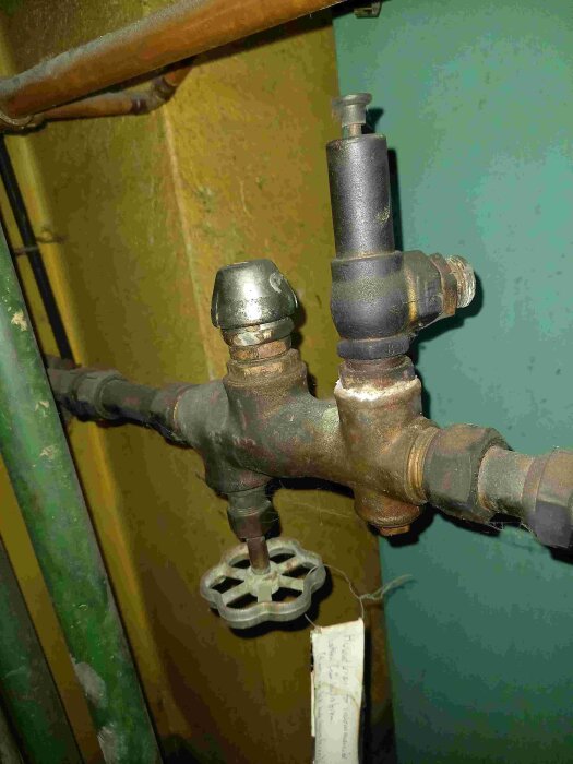 VVS-komponenter på en oljepanna från 1980 med kranventil och säkerhetsventil; obeskriven kromad del som ibland sprutar vatten.