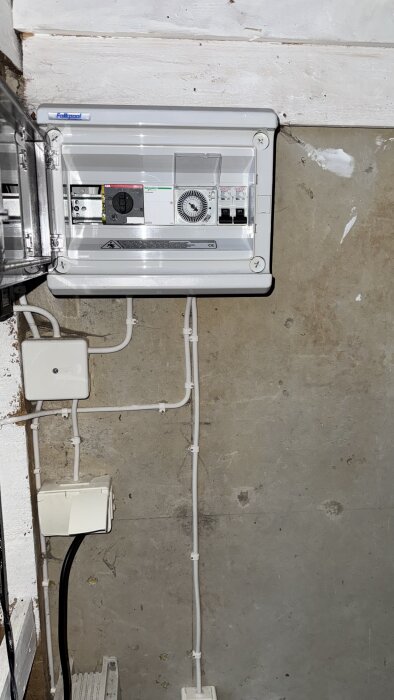 Elcentral med tidrelä och brytare, monterad på en vägg med synliga kablar.