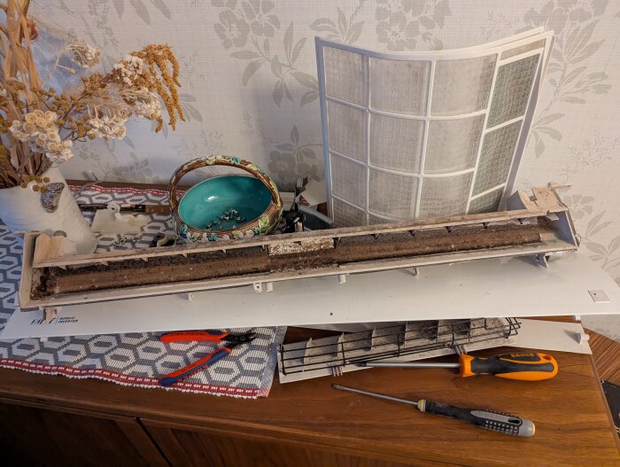 Demonterad luftkonditionering med smutsiga filter på ett bord, omgiven av verktyg och en korg.