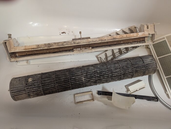Delar av en smutsig och isärplockad luftkonditionering ligger i ett badkar för rengöring.