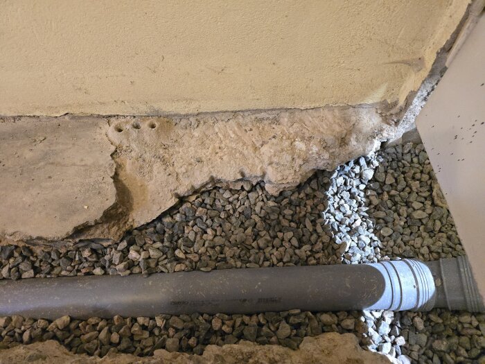 Betongyta med markeringar och exponerat avloppsrör i stambytesprojekt, omgivet av makadam i hobbyrum.