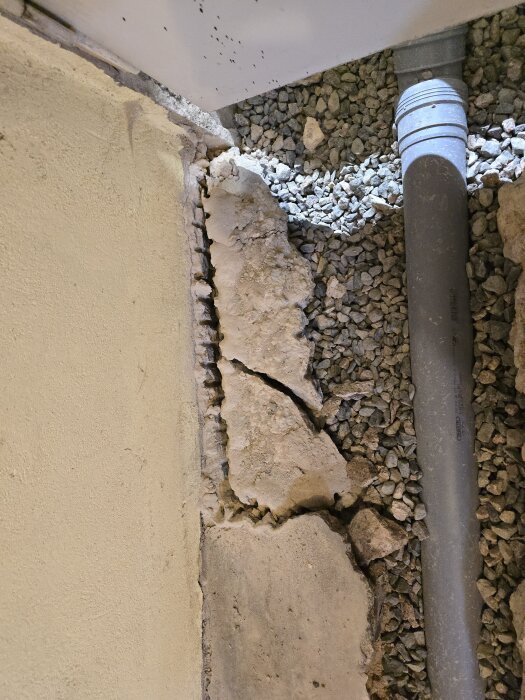 Betongytan och ett avloppsrör i en renoveringszon, omgivna av grus och spruckna betongfragment.