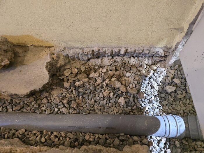 Bruten betongyta i hörnet av ett hobbyrum med exponerat grus och avloppsrör inför reparation och stambyte.