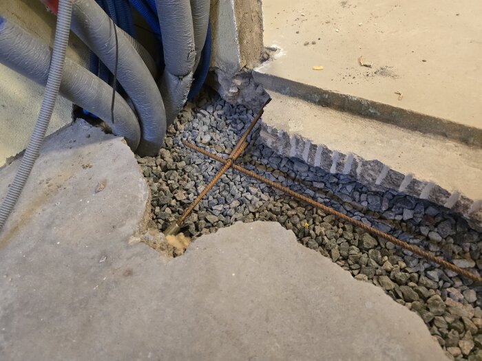 Grusfylld ränna med armeringsjärn och synliga rör i ett hobbyrum, förberett för gjutning av betong.