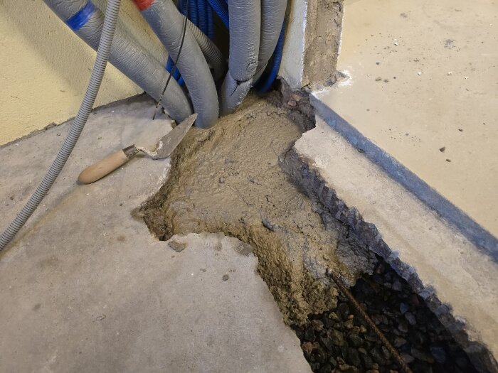 Betonggjutning i ett golv där en ränna fylls. Verktyg och VVS-rör i bakgrunden.