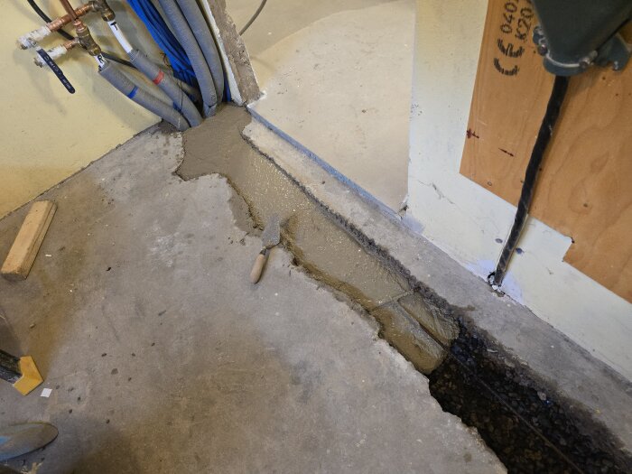 Betong lagd i golvränna i hobbyrum. Verktyg vid sidan för att jämna ut ytan. Rör och ledningar syns längs väggen. Arbete pågår.