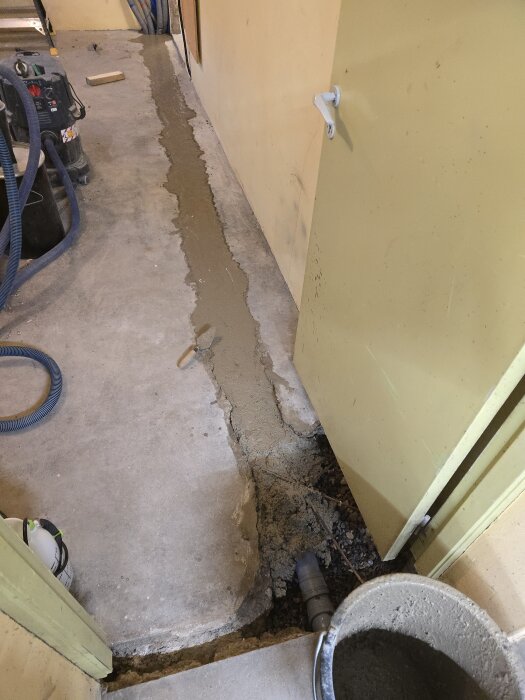 Betongränna i hobbyrum under gjutning med utrustning och hink fylld med betongmassa i närheten, del av pågående renoveringsprojekt.