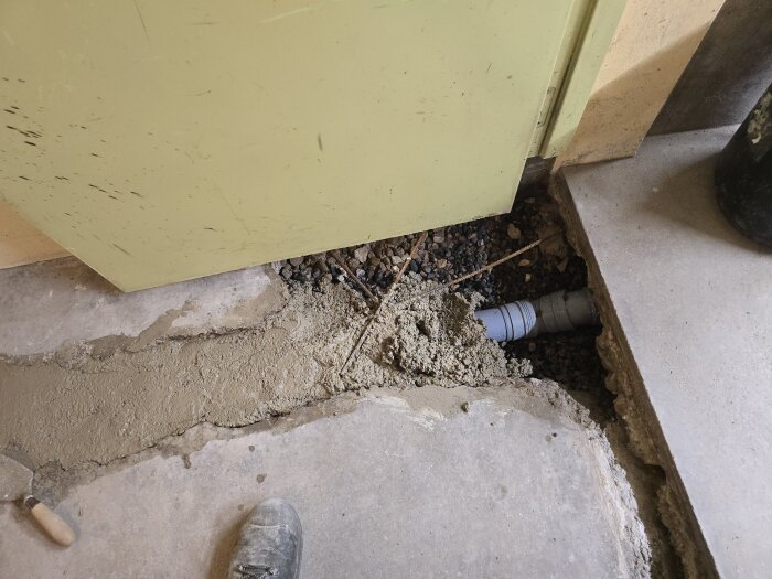 Gjutning av betongränn i hobbyrum, visar ett delvis täckt avloppsrör och nygjuten betong med en putsbräda i närheten.