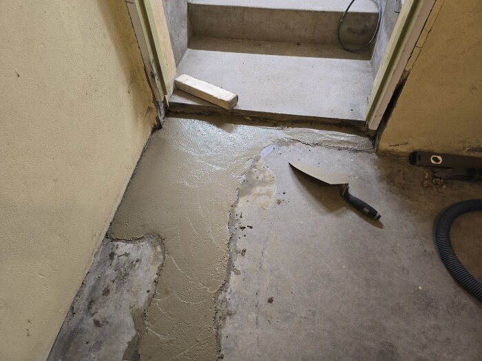 Betongarbete i hobbyrum, med nylagt betong i ränna vid en dörröppning. En murslev och ett vattenpass ligger på golvet.
