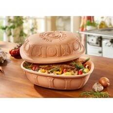 Oglaserad lergryta på ett köksbord, fylld med grönsaker och örter. Locket är avtaget och placeras ovanpå.