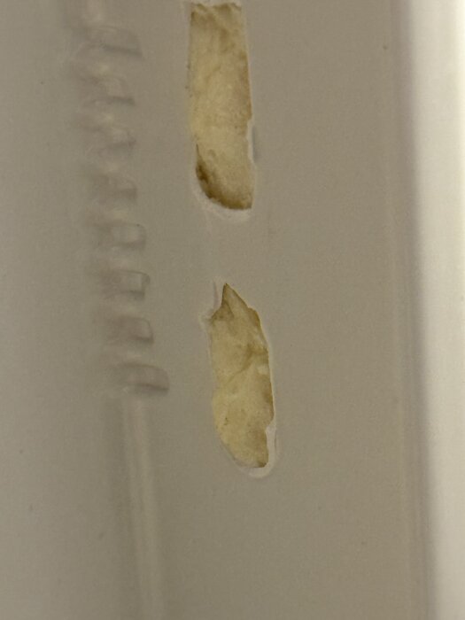 Skada i kylskåpsdörrens insida där fäste för hylla har lossnat, synlig beige isolering.