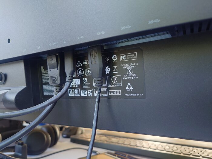 Baksidan av en datorskärm med flera anslutna kablar i olika portar, inklusive en USB-kabel som är kopplad till en inbyggd USB-hubb.