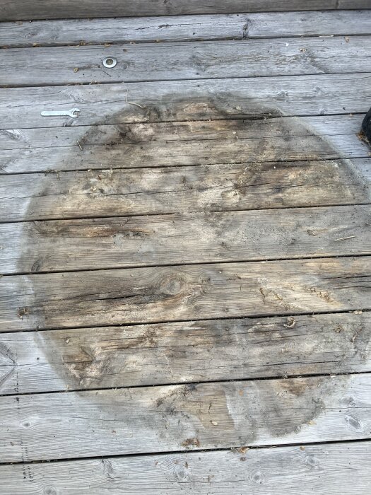 Murken träterrass med rund avtryck från parasollfot och sprickor.