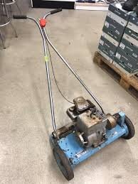 Bensingräsklippare med öppen cylinder och snurrande knivar framtill, liknande en gammal Husqvarna-modell, stående på ett betonggolv.