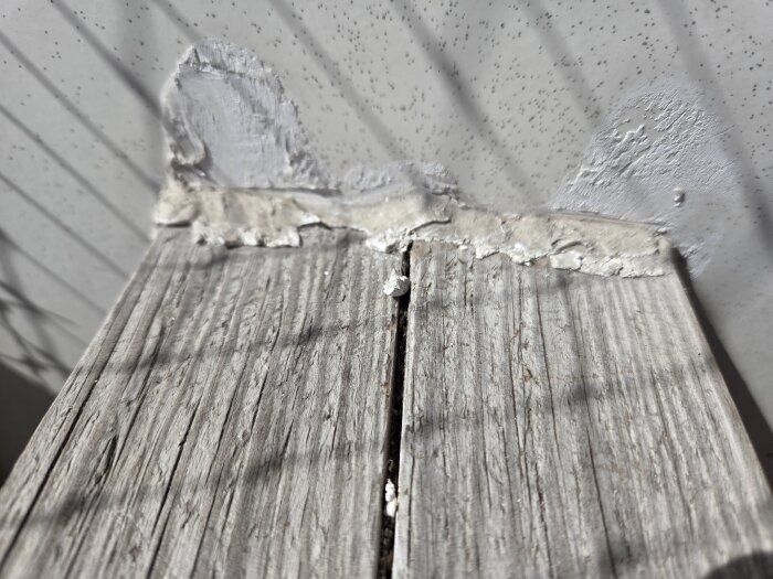 Gammalt trä med vitt lim eller spackel applicerat mot metall, vilket visar slitage och sprickor i ytan. Solens skugga över arbetsytan.