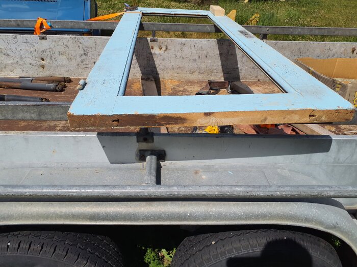 Blå dörrkarm ligger på en bilsläpvagn, troligen för renovering. Verktyg och en kartong syns i bakgrunden.