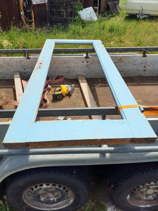 Gammal blå dörr på en släpvagn med verktyg bredvid, redo för demontering och installation av ny panel.