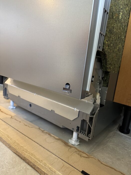 Diskmaskinens undersida där fjädrarna syns, installerad på golv med träplatta.