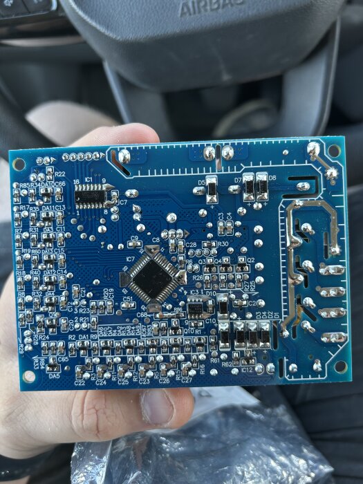 Närbild av ett kretskort med olika komponenter monterade på en blå bakgrund, hålls i en hand.
