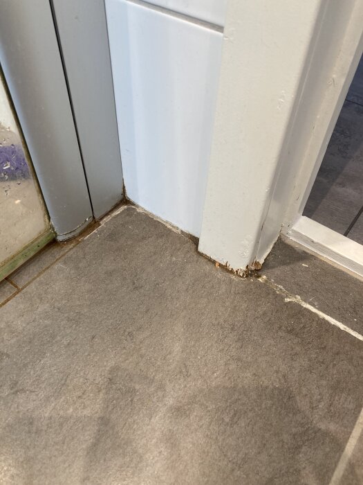 Dörrkarm i ett badrum med synliga fuktskador och blött fodermaterial nära klinkergolv och dusch.