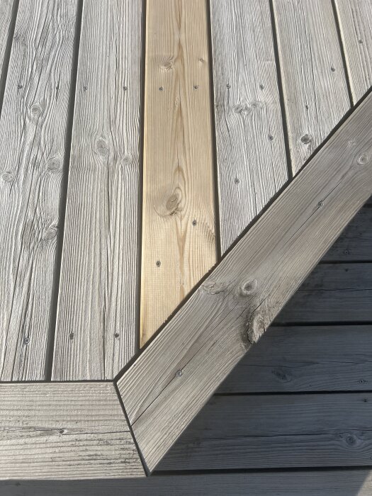 Ny trallbräda med ljus färg bredvid äldre, gråare träbrädor på en altan. Färgskillnaden visar på byte och underhåll av trall.