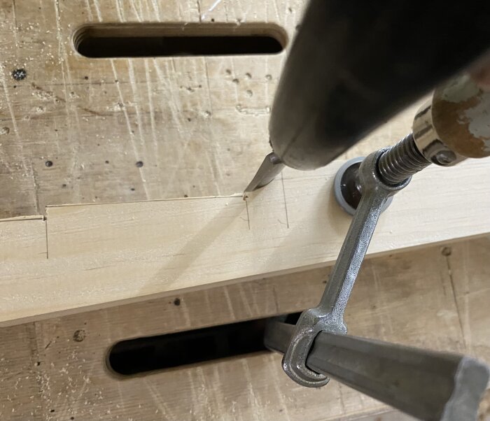 Närbild av träbit fastspänd med metalltvingar på arbetsbänk, snitt sågas med Japansåg enligt instruktioner för att passa profiler mot dörrar.