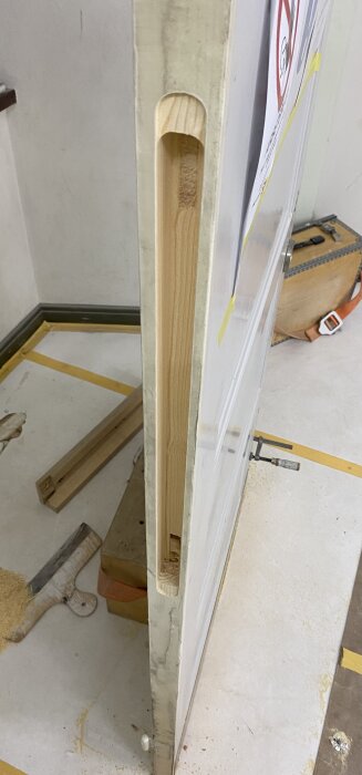 Utsågad dörrkarm med synliga trälister och håluttag för automatiker. Verktygskista och sågspån i bakgrunden.