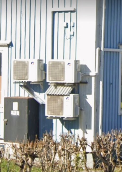 Utedelar av luftkonditioneringssystem på blå fasad, med gasolskåp under en av enheterna.