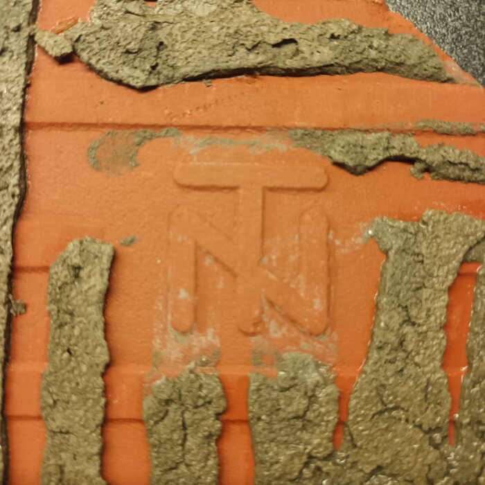 Klinker med inpräglat märke "TN" synligt under bortskrapat material.